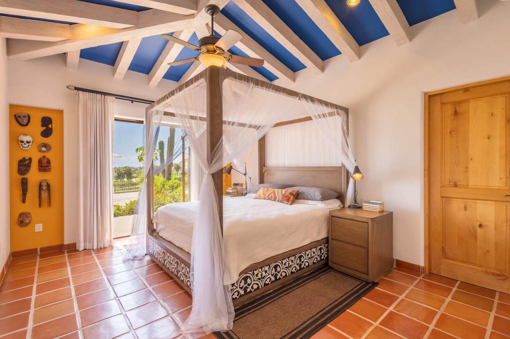 Luxurious bedroom with canopy bed, terracotta tile floors, blue beamed ceiling, and outdoor terrace view at Casa Luna Escondida Palmilla.