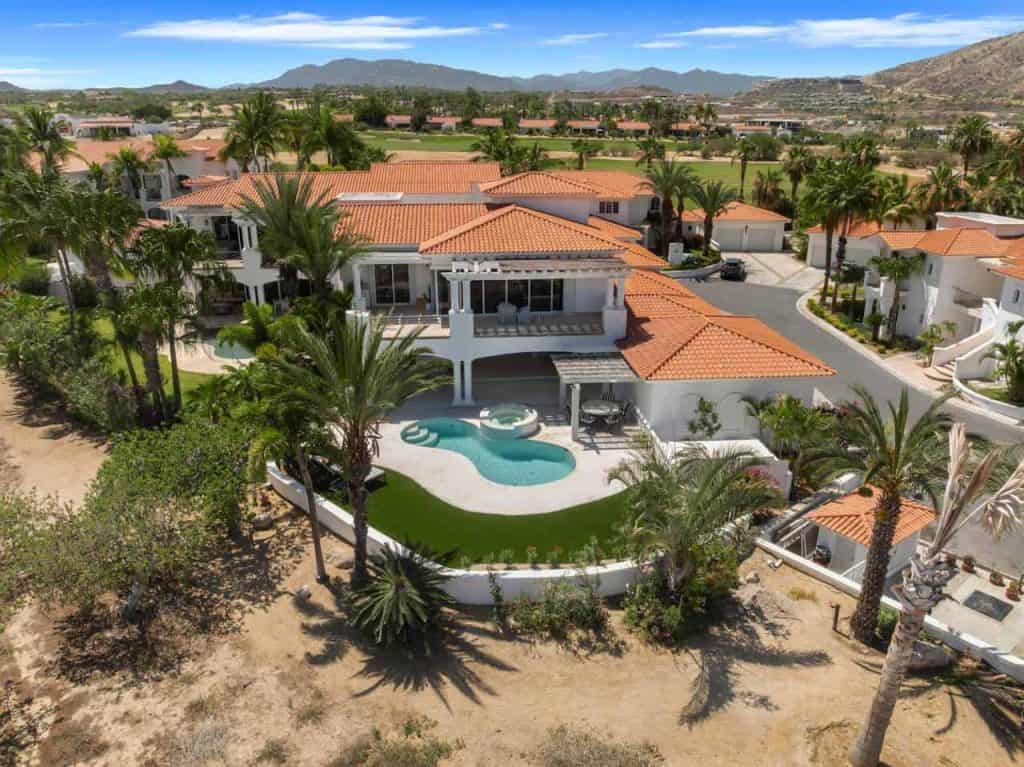 Pool Area With Hot Tub And Manicured Lawn Overlooking The Ocean, Within A Luxurious Golf Community With Scenic Mountain Views In The Background.