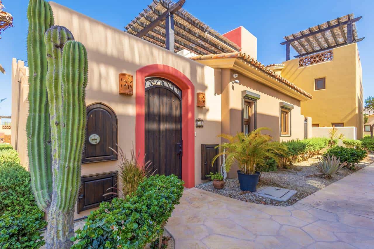 Vibrant Exterior View Of A Coastal Golf Community Home At Club Campestre, Showcasing Lush Desert Landscaping, A Large Cactus, And Colorful Architectural Details With Ocean View In The Background.