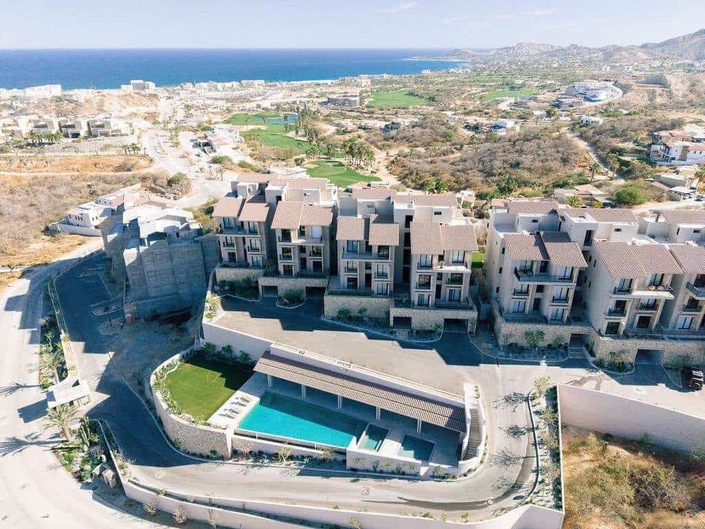 Aerial View Of A Luxury Golf Community With Ocean Views, Featuring Modern Residential Buildings, A Swimming Pool, And Scenic Landscape In The Background.