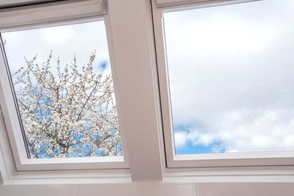 Skylights Installation services in Cape Cod- A modern open skylight,mansard window against blue sky with beautiful tree with white flowers, modern new house design, architectural detail