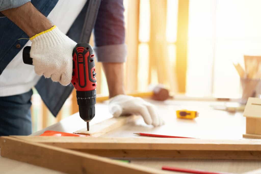 Carpentry Services in Cape COD - Hands of carpenter uses hand drill to assemble the wood in the carpentry shop