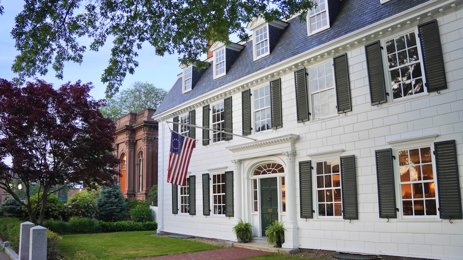 White New England colonial home with dark shutters showing classic siding and trim color contrast