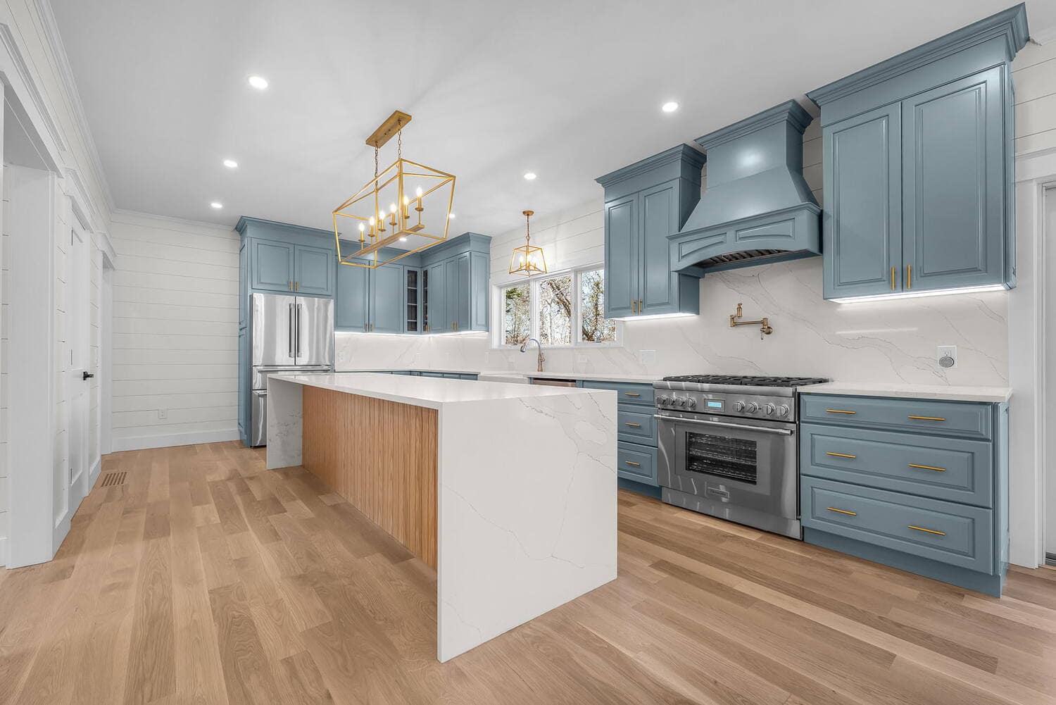 Coast Carpentry Home Group finished kitchen remodel on Cape Cod with coastal blue cabinetry, a quartz waterfall island, and white oak floors
