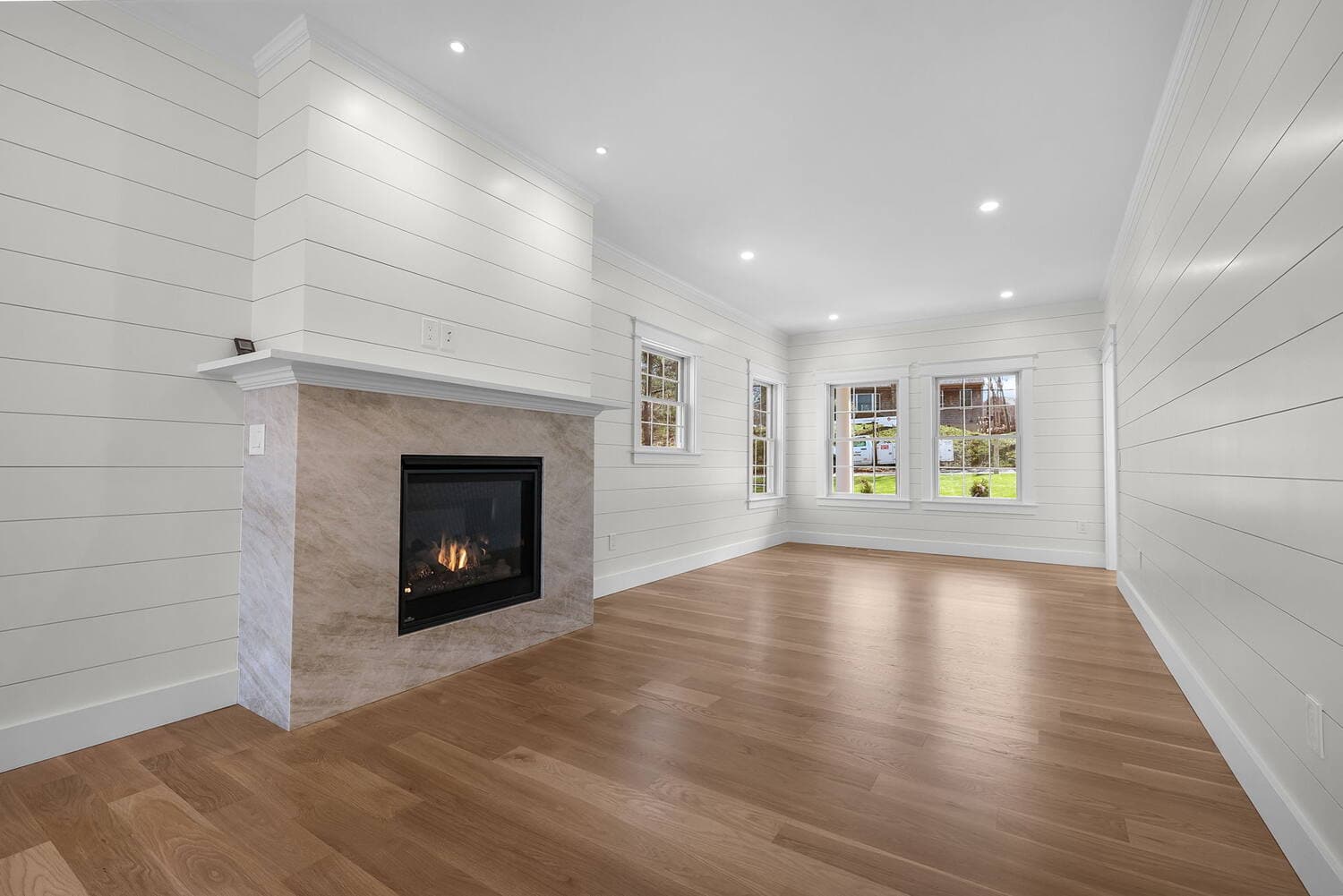 Finished living room by Coast Carpentry in a Cape Cod home with shiplap walls, crown molding, a custom fireplace mantel and white oak floors