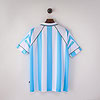 Camiseta de fútbol Argentina azul y blanca, estilo vintage, colgada en pared blanca.