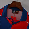 Camisa de fútbol del FC Barcelona con logo Kappa, en tonos azul y rojo, colgada en percha de madera.