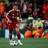Jugador de fútbol en acción durante un partido de la UEFA Champions League, vistiendo el uniforme del Liverpool FC.