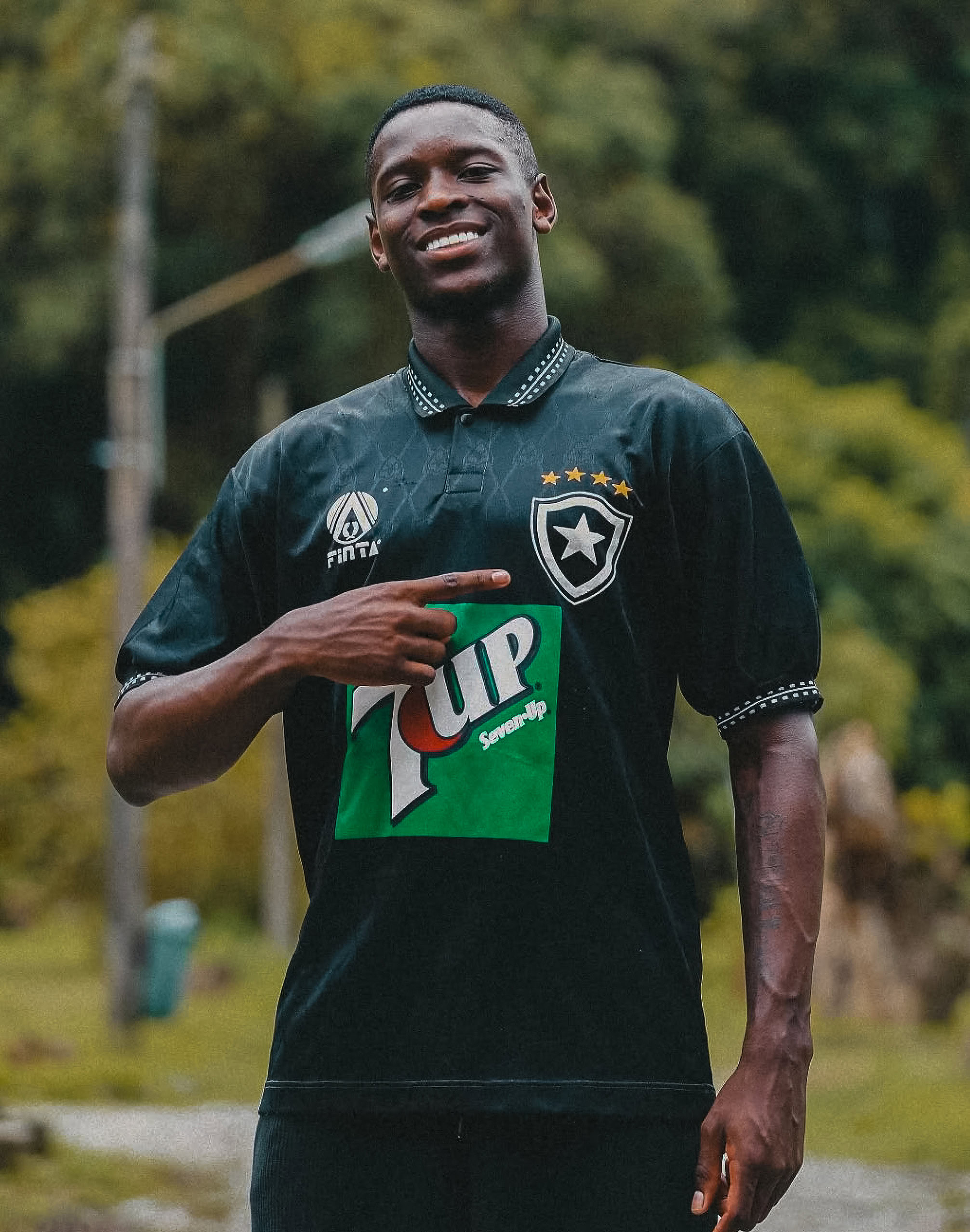 Camisa de fútbol con logo y patrocinador, deportista sonriendo en campo abierto, estilo deportivo y moda deportiva.