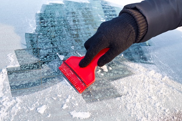 Technician cleaning ice and snow off a car windshield with a brush.