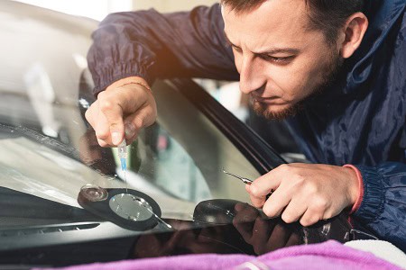 Technician repairing car windshield with calibration tools.