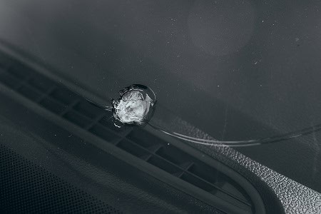 Damaged windshield with cracked glass and calibration sensor.