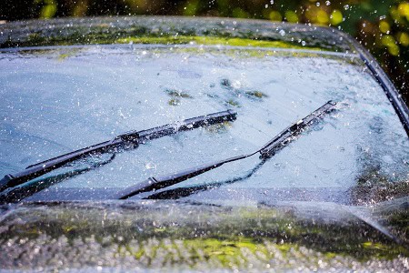 Car windshield with broken wipers during rain, auto glass repair service.