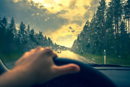 Driver's view on a rainy day with windshield wipers in action.
