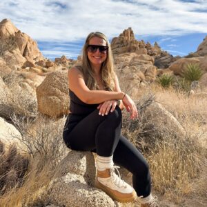 Woman sitting on a rock in a desert landscape with mountains in the background.