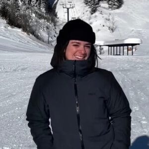 Woman smiling in winter jacket and hat in snowy landscape.
