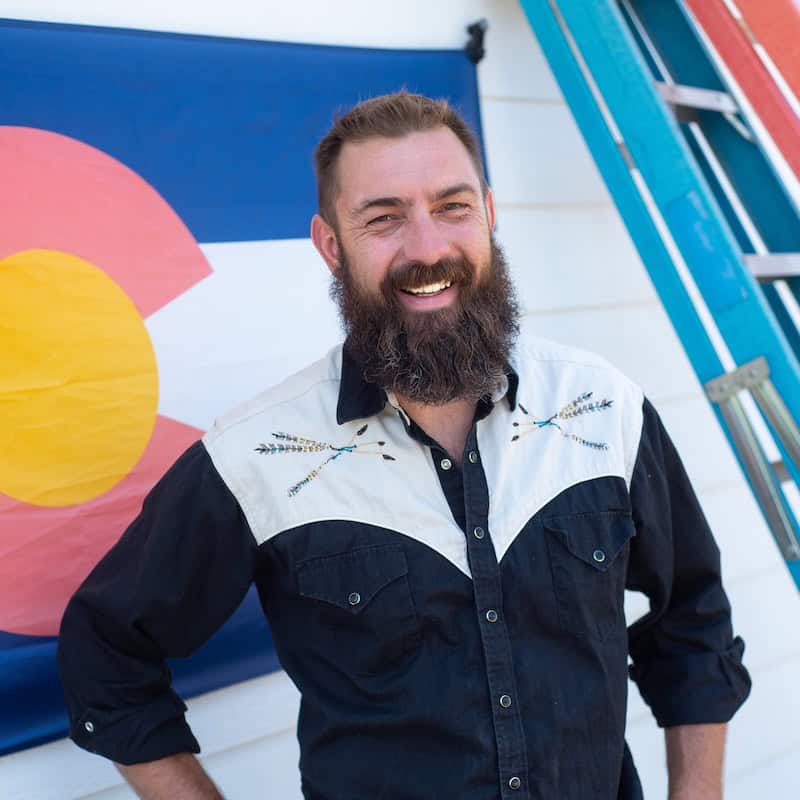 Man with a beard smiling outdoors in front of Colorado-themed decor.
