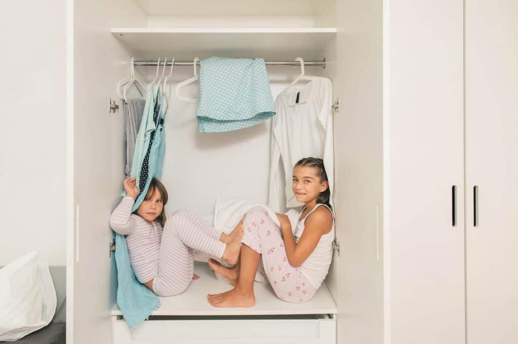 Kids sitting inside a custom closet with hanging clothes and storage solutions.