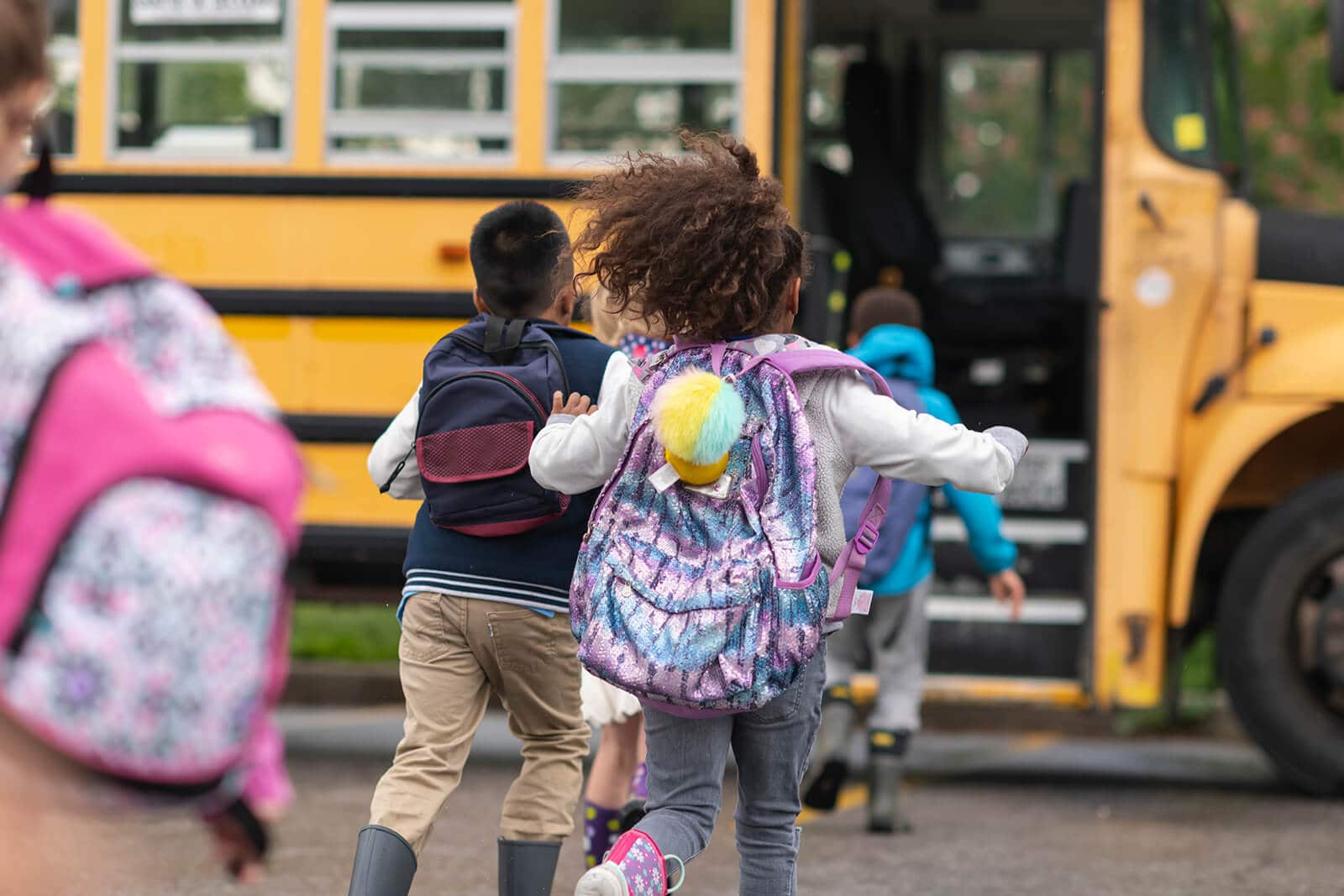 Kids with backpacks running towards a school bus.