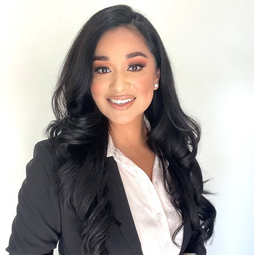 Young woman real estate agent with long black hair and professional attire smiling confidently.