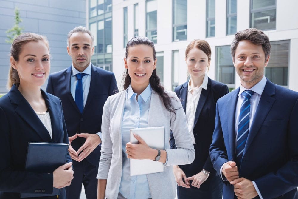 Diverse real estate team of professionals standing outdoors in business attire.