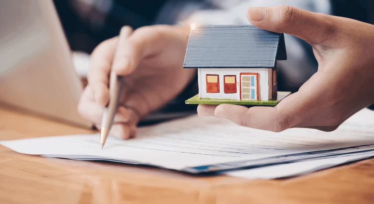 Real estate agent holding a miniature house model, reviewing documents for home buying or selling.