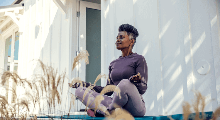 Meditating woman practicing yoga outdoors in front of a white building, promoting wellness and relaxation.