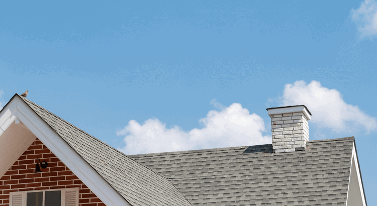 Roof of a residential home with a chimney against a blue sky.