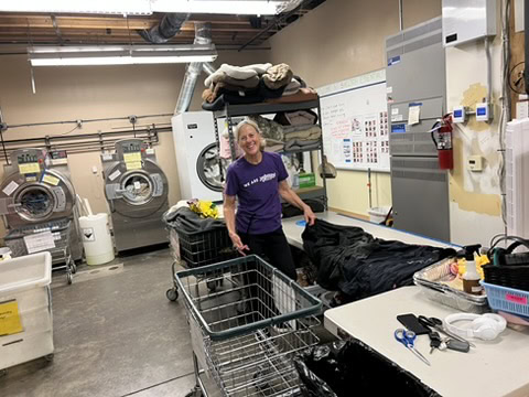 Widely smiling woman laundry worker in a commercial laundry facility, handling laundry bags and shopping carts.