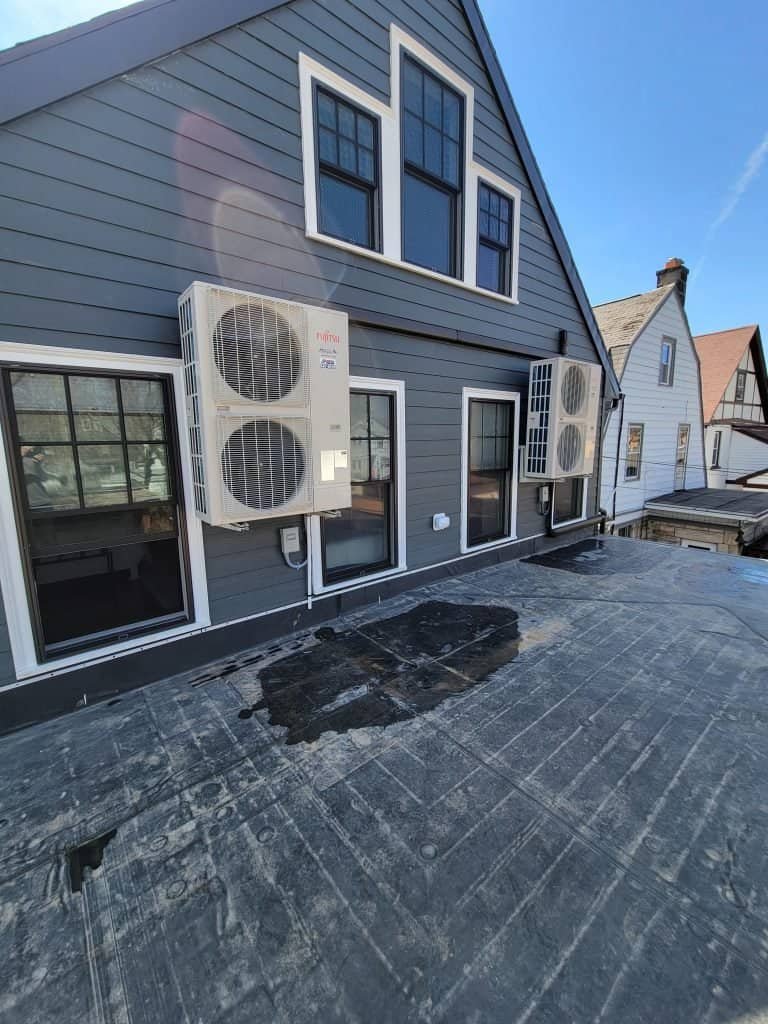 JP Heating & Cooling air conditioning units installed on a homes roof in Buffalo, NY. Black marks beneath units suggest possible leakage or wear.