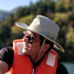 Smiling man in a sun hat and orange life vest outdoors, customer testimonial avatar