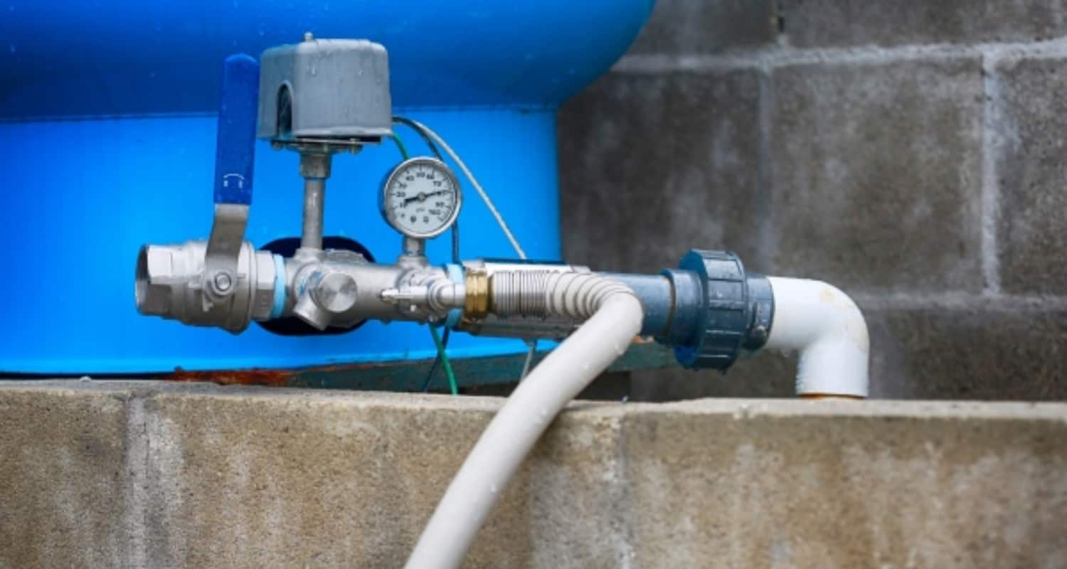 Blue water tank plumbing system with pressure gauge and white PVC pipe for residential or commercial water management.