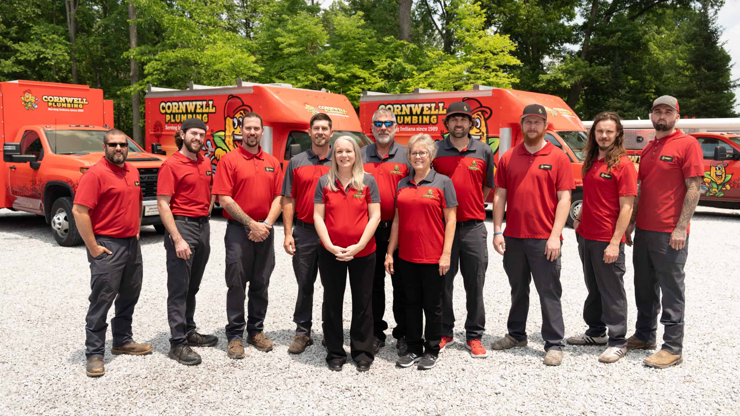 Team of professional plumbers from Cornwell Plumbing standing outdoors with service trucks, ready to provide plumbing repairs and installations in Indiana, emphasizing expert plumbing services and team reliability.