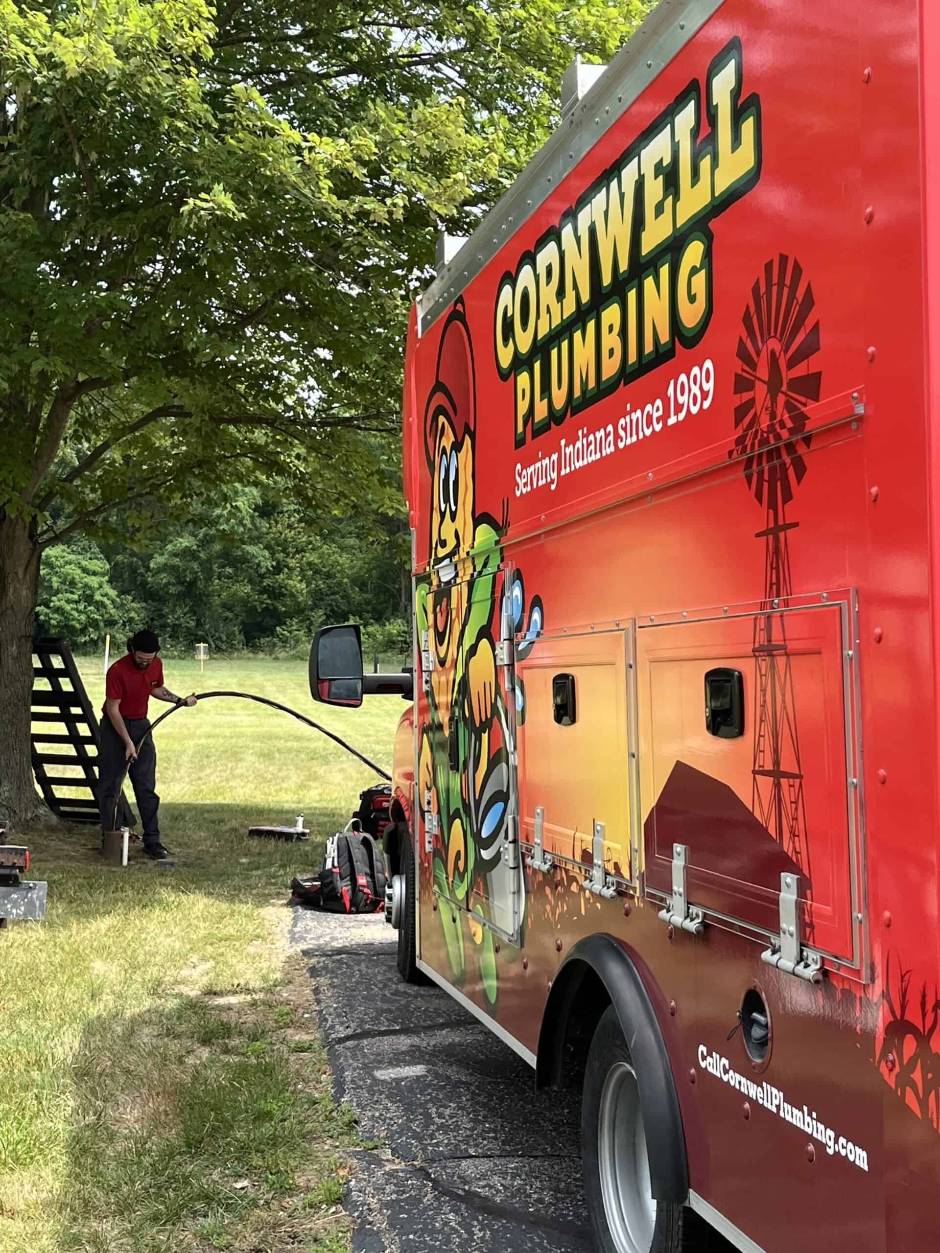 Service truck with Cornwell Plumbing branding and a colorful mascot, parked outdoors under a tree on a sunny day.