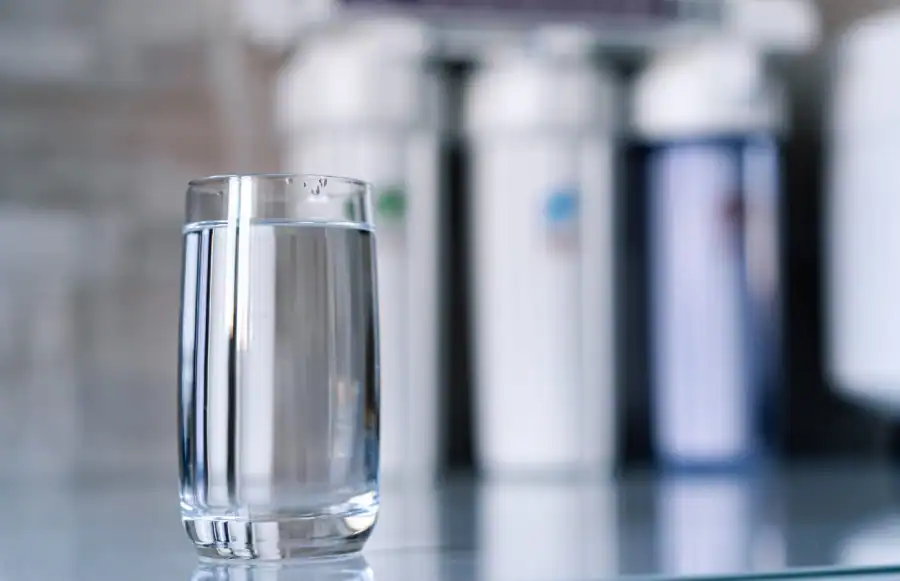 Clear drinking water glass in front of water filtration system for clean water supply.