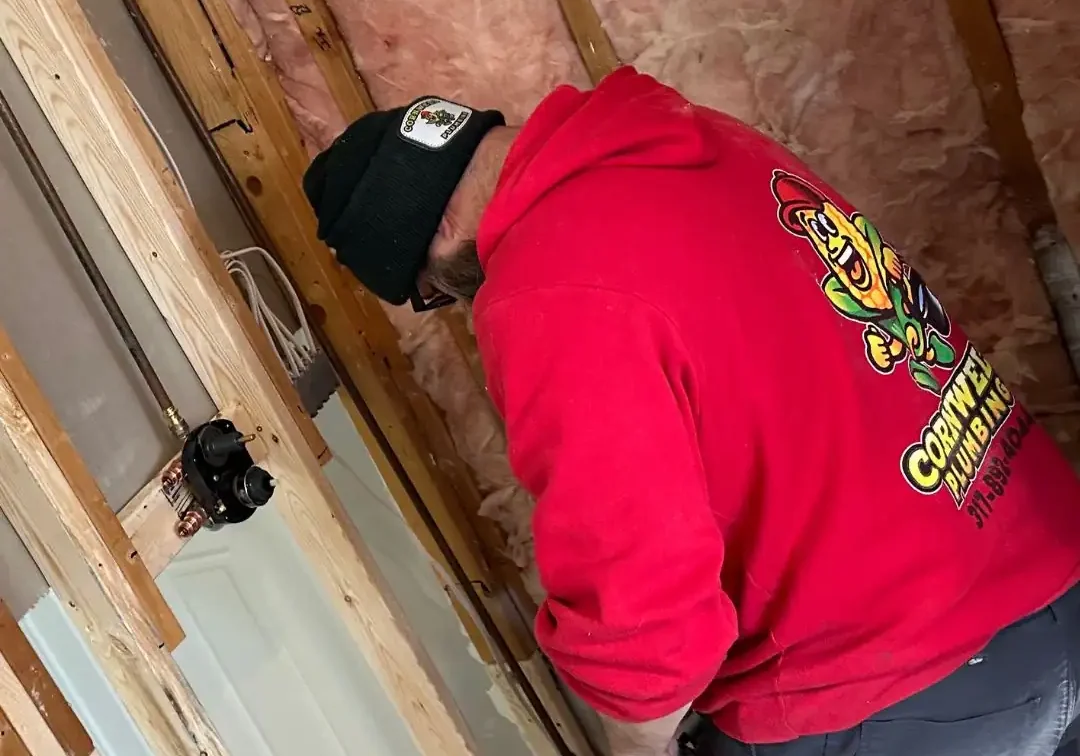 Repairing plumbing and pipes inside a wall, expert plumber from Cornwell Plumbing in action, professional plumbing services, residential plumbing repair, skilled plumber working on pipe installation.