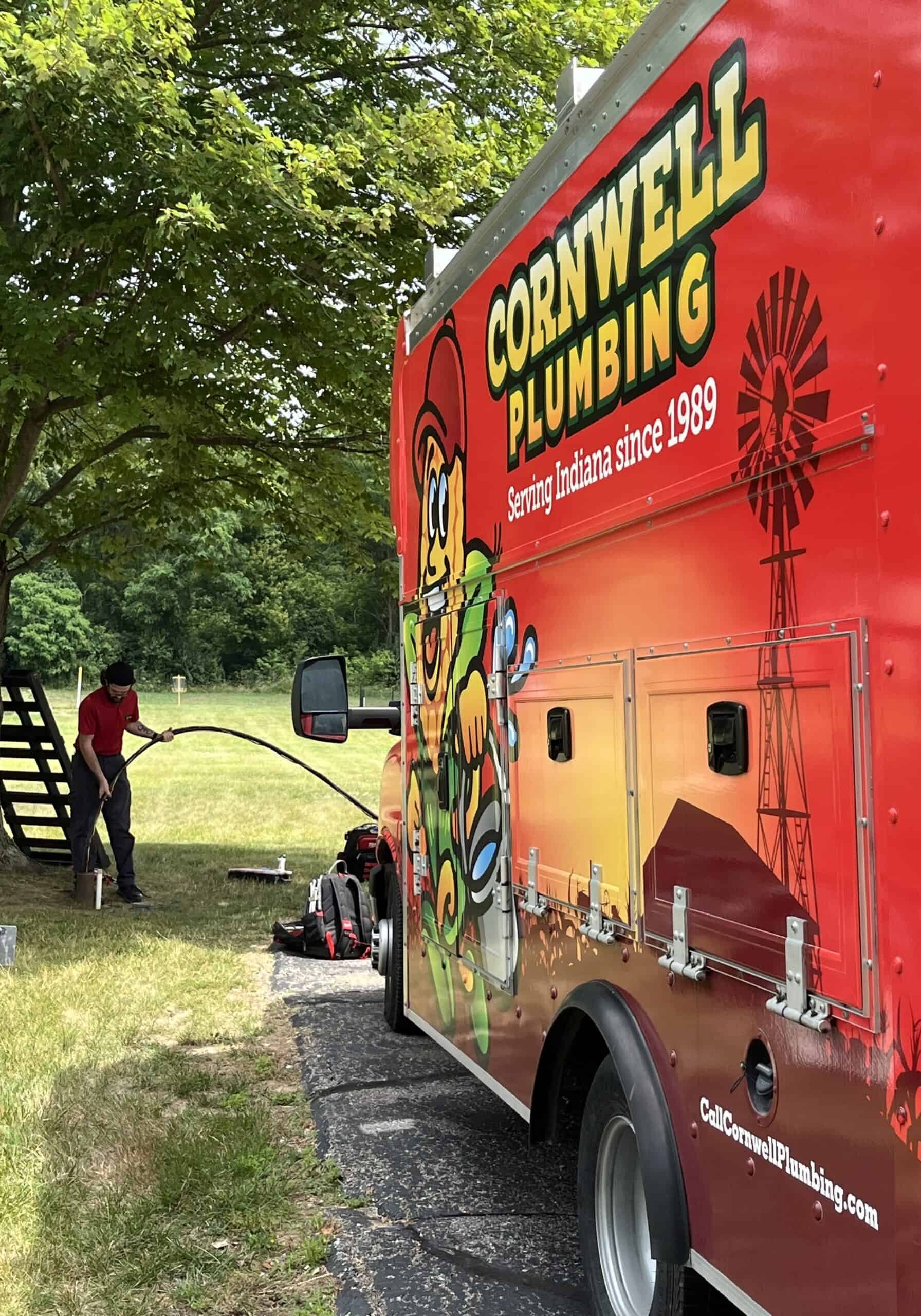 Service truck with Cornwell Plumbing branding and a colorful mascot, parked outdoors under a tree on a sunny day.