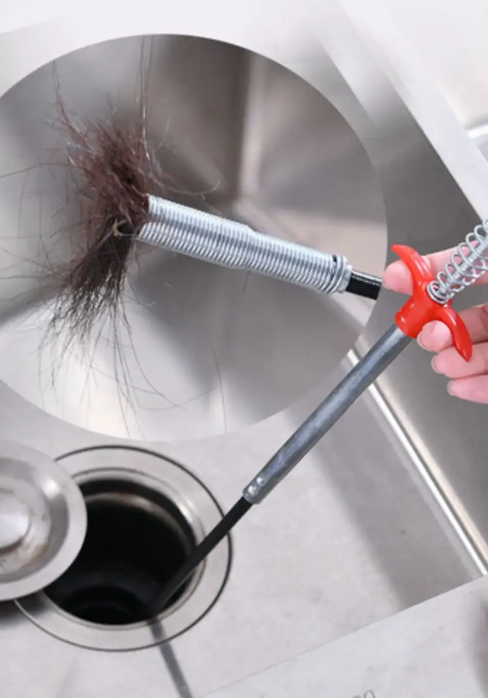 Clogged drain cleaning with plumbing snake in stainless steel sink, hair removal service.