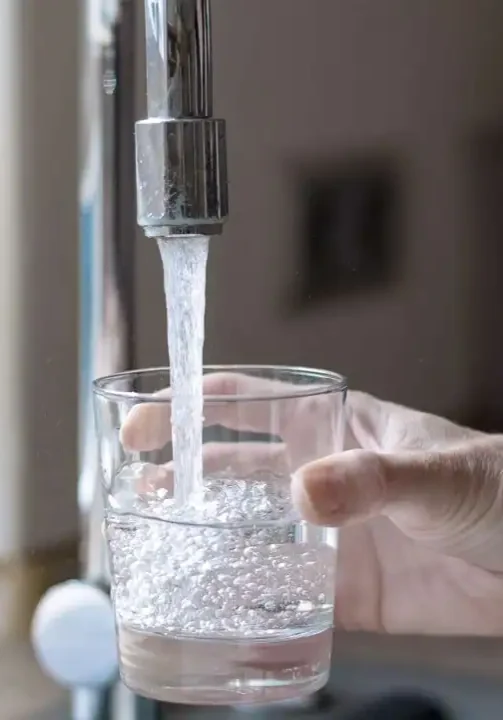 Water flowing from a kitchen faucet into a glass, showing the importance of professional plumbing services.