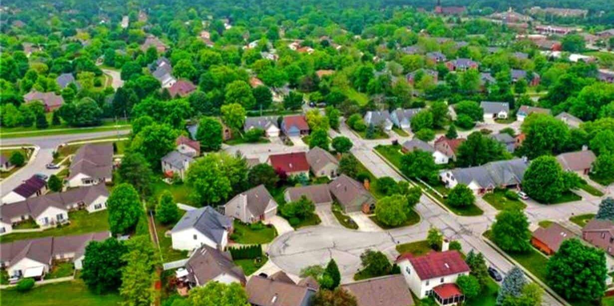 Aerial view of a suburban neighborhood with green trees, residential houses, and streets, showcasing a peaceful community setting.
