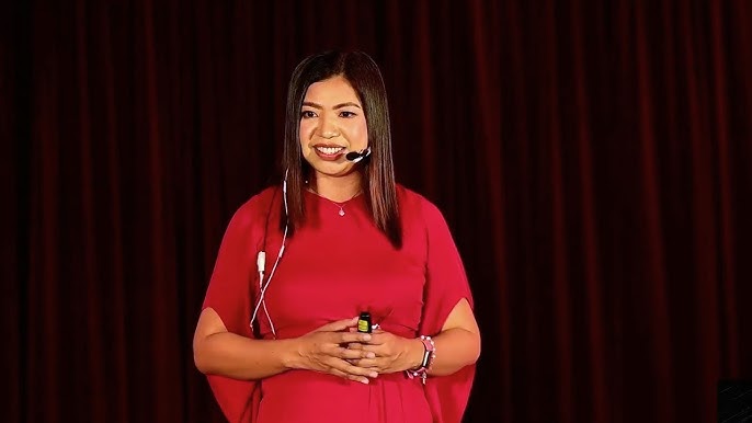 Sha Nacino speaking on stage in a red dress