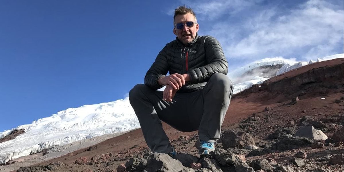 Tim Jarvis crouched on volcanic terrain near a glacier