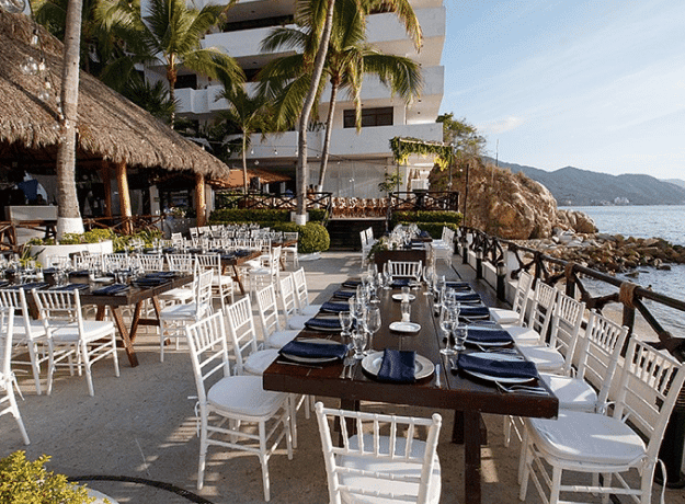 A beach wedding setup featuring white tables and chairs arranged elegantly on the sand with ocean waves in the background.
