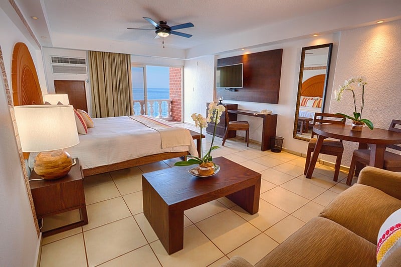 A hotel room featuring a bed, a television, and a balcony with natural light streaming in.