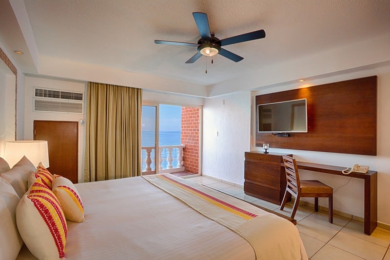 A hotel room featuring a bed, television, and a balcony with a view of the ocean.