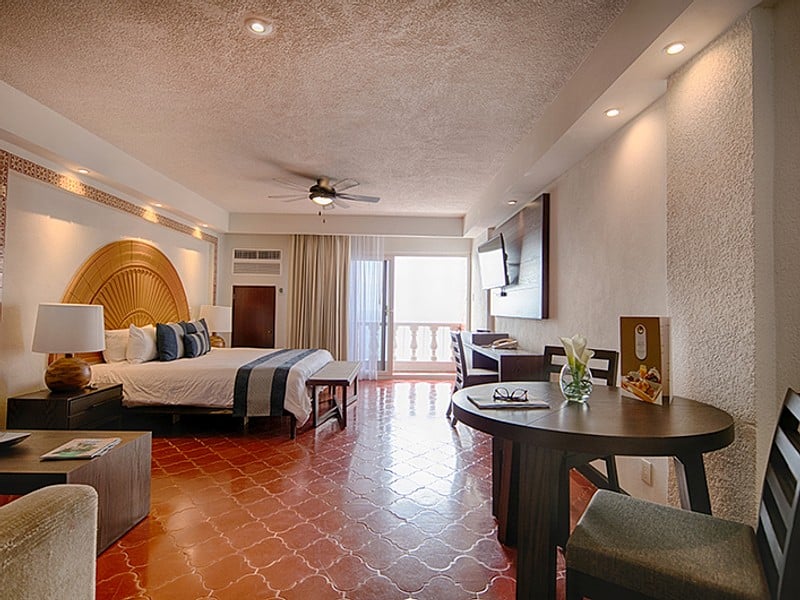 A hotel room featuring a bed, a television, and a balcony with natural light streaming in.