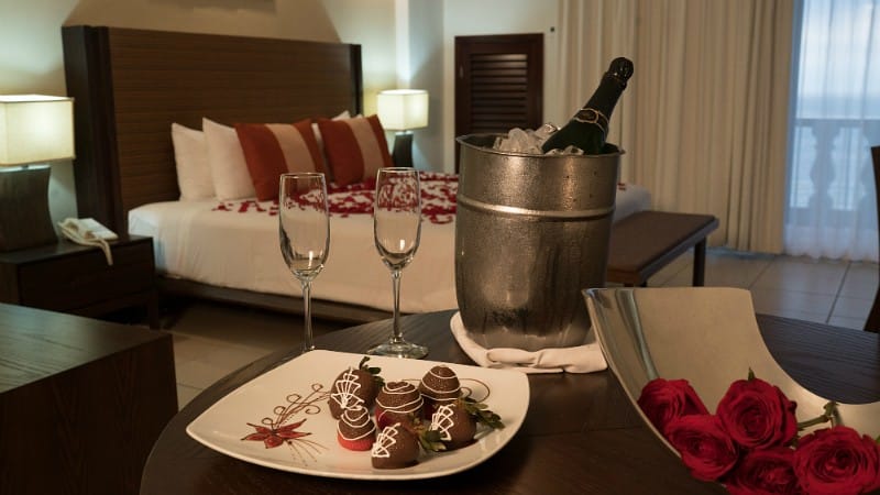 A cozy room featuring a bed, two champagne glasses, and a plate of chocolates, creating a romantic atmosphere.