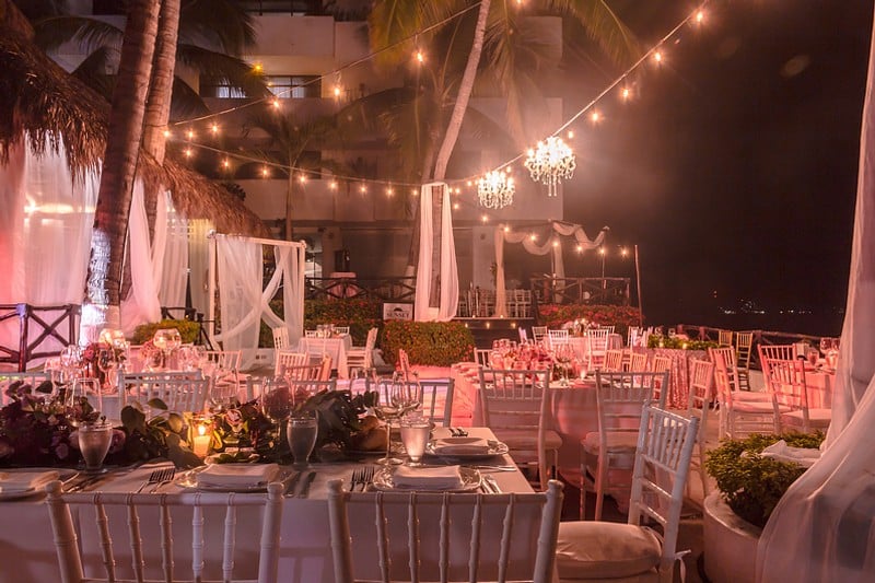 A wedding reception featuring elegant white linens and soft pink lighting, creating a romantic atmosphere.