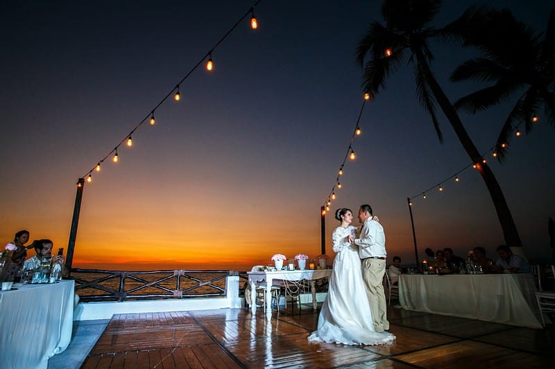 A bride and groom share their first dance together at sunset, surrounded by a warm, golden glow.