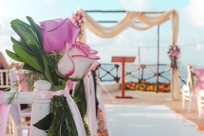 A picturesque wedding ceremony on a beach in Cancun, with guests seated under a floral arch and the ocean in the background.